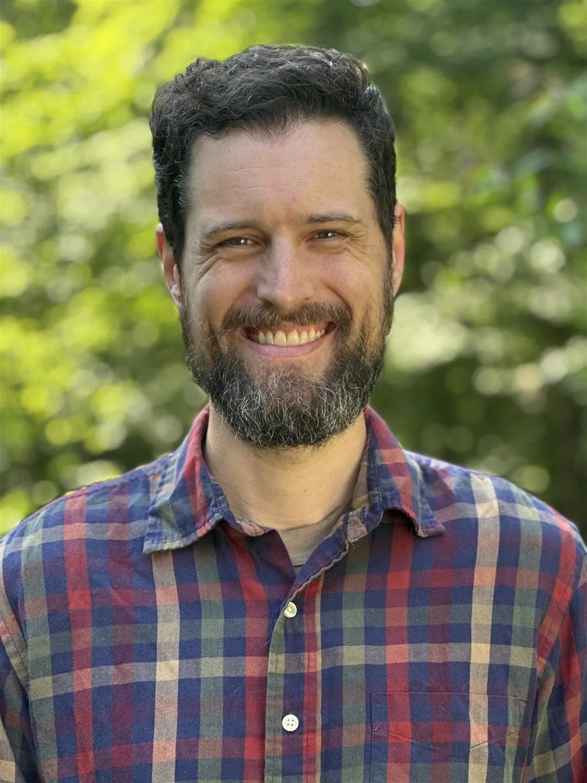 Sam Deering smiling outdoors in a plaid shirt